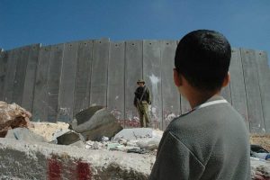 A Palestinian boy and an Israeli soldier by Israel's illegal separation wall in the West Bank. (Justin McIntosh/CC BY 2.0)
