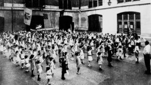 Students being indoctrinated into the state religion give the "Bellamy salute" toward the US flag while reciting the "Pledge of Allegiance", written by Francis Bellamy. (New York Tribune/Public Domain)